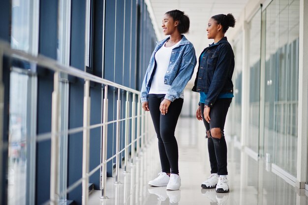 Due amiche africane in giacca di jeans poste insieme al coperto