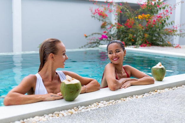 Due amiche asiatiche e caucasiche della donna con il trucco nella piscina alla villa