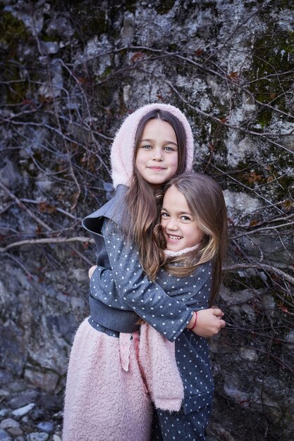Due amiche carine che si abbracciano su uno sfondo di pietra grigia.