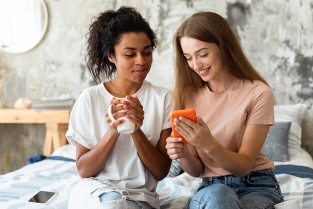 Due amiche che esaminano smartphone mentre sorseggiano un drink