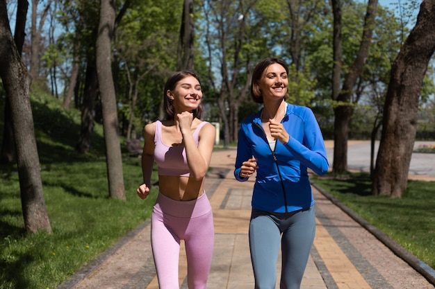 Due amiche felici positive che corrono insieme a fare jogging nel percorso del parco sorridono e ridono