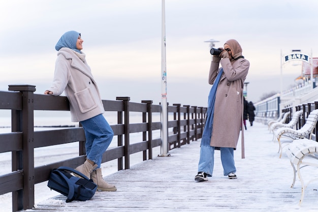 Due amiche musulmane che scattano foto in riva all'oceano mentre viaggiano