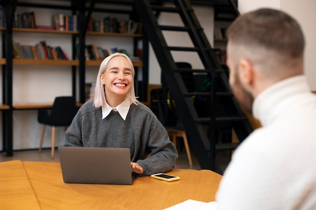 Due amici che studiano usando i taccuini e un computer portatile in una biblioteca