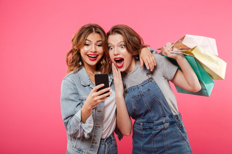 Foto gratuito due amici colpiti delle donne che tengono i sacchetti della spesa facendo uso del telefono cellulare.