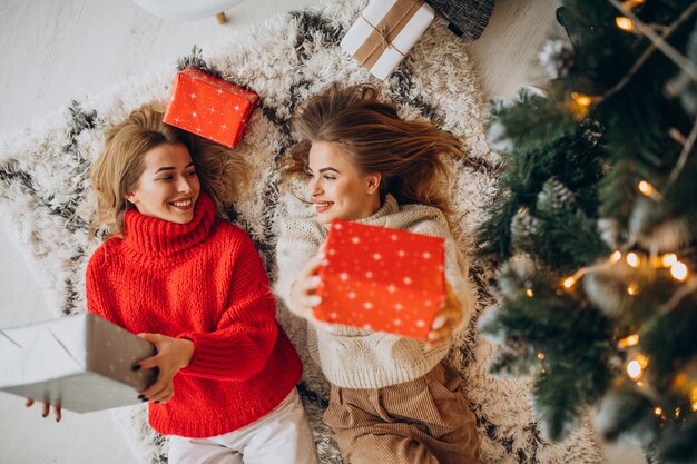 Due amici di ragazze che si siedono con i regali di Natale dall'albero