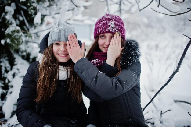 Due amici di ragazze divertenti che si divertono in una giornata nevosa invernale vicino ad alberi innevati