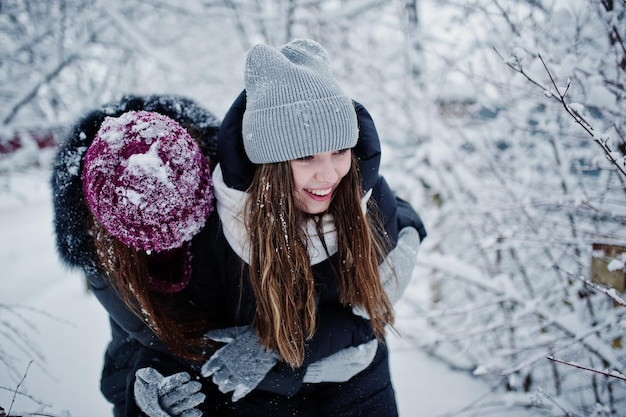 Due amici di ragazze divertenti che si divertono in una giornata nevosa invernale vicino ad alberi innevati