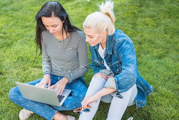 Due amici femminili che si siedono sull&#39;erba verde facendo uso del computer portatile