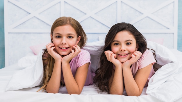 Due amici femminili sorridenti che si trovano sotto il lenzuolo che guarda alla macchina fotografica