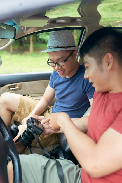 Due amici maschii asiatici che si siedono in automobile e che controllano le foto sulla macchina fotografica digitale