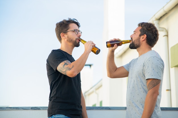 Due amici maschii che godono della birra sul terrazzo all'aperto