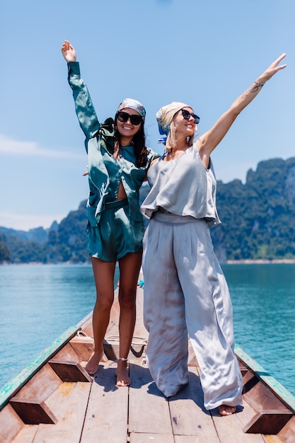 Due amici turisti blogger donna felice in vestito di seta e sciarpa e occhiali da sole in vacanza viaggiano intorno alla Tailandia sulla barca asiatica, parco nazionale di Khao Sok.