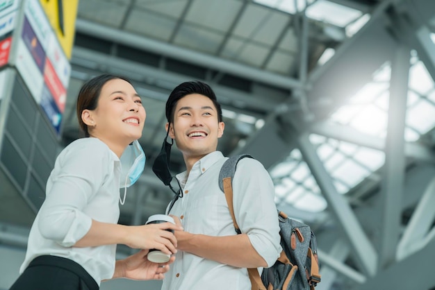 Due attraenti uomini d'affari asiatici e una donna d'affari con la mano salutano e salutano l'allontanamento sociale nel terminal dell'aeroporto di partenza