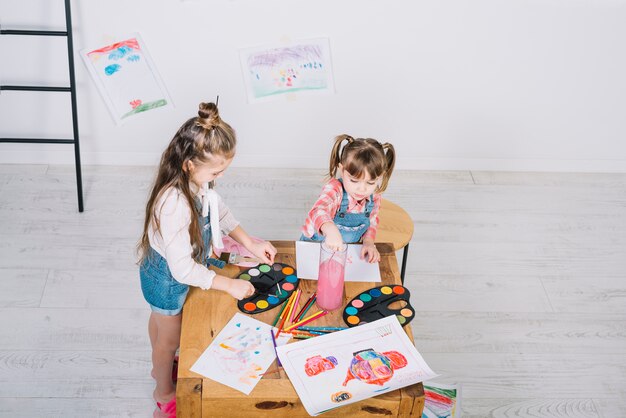 Due bambine che dipingono con aquarelle al tavolo di legno