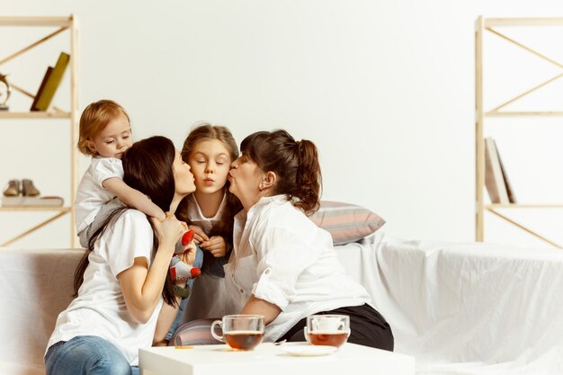 Due bambine la loro giovane madre attraente e la loro nonna affascinante seduta sul divano e trascorrere del tempo insieme a casa. Generazione di donne. Giornata internazionale della donna. Buona festa della mamma.