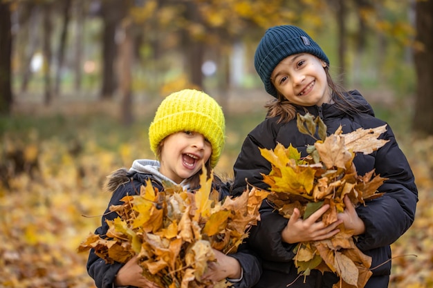 Due bambine stanno giocando tra le foglie d'autunno per una passeggiata nella foresta