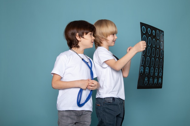 Due bambini adorabili adorabili dolci in magliette e jeans bianchi che guardano raggi x sullo scrittorio blu