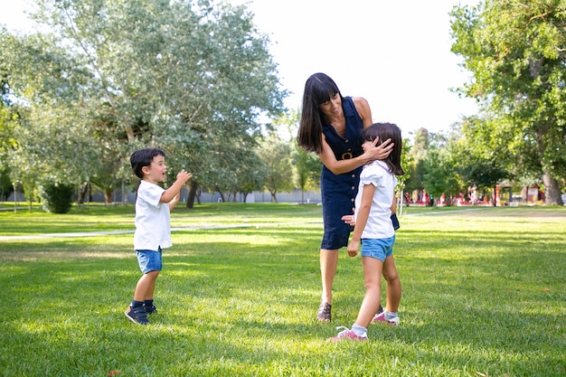 Due bambini carini felici e la loro mamma che trascorrono il tempo libero nel parco estivo, in piedi sull'erba, godendo delle attività. Concetto di famiglia all'aperto