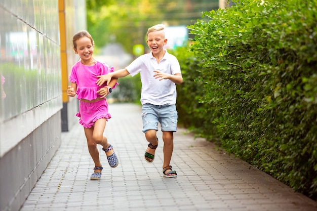 Due bambini sorridenti, ragazzo e ragazza che corrono insieme in città, città nel giorno d'estate