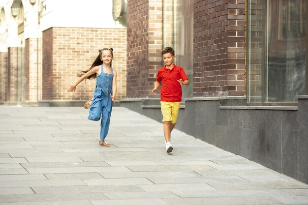 Due bambini sorridenti, ragazzo e ragazza che corrono insieme in città, città nel giorno d'estate