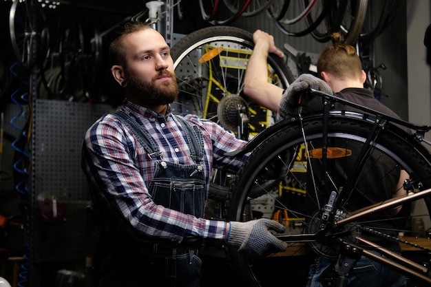 Due bei maschi alla moda che lavorano con una bicicletta in un'officina. I lavoratori riparano e montano la bici in un'officina.