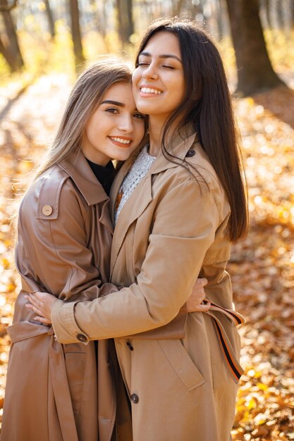 Due belle amiche che trascorrono del tempo insieme. Due giovani sorelle sorridenti che camminano nel parco d'autunno e si abbracciano. Ragazze brune e bionde che indossano cappotti.