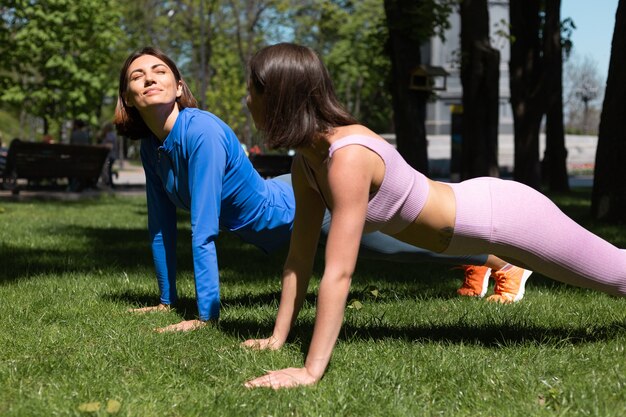 Due belle donne in abbigliamento sportivo sull'erba nel parco al giorno pieno di sole facendo impianto di allenamento si sostengono a vicenda emozioni felici