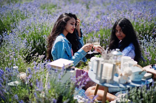 Due belle ragazze indiane che si siedono in un campo di lavanda viola con decorazioni con gli occhiali in mano