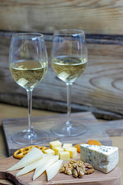 Due bicchiere di vino bianco con tagliere di formaggi su rustico con vari formaggi, gorgonzola, gauda e noci e snack