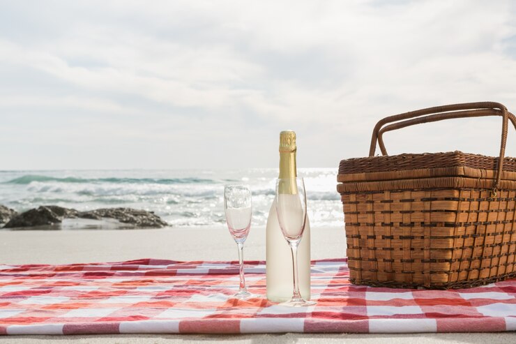 Due bicchieri, bottiglia di champagne e cesto da picnic sulla spiaggia coperta