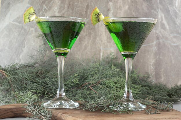 Due bicchieri di cocktail verde con fette di kiwi su tavola di legno.