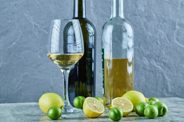 Due bottiglie e un bicchiere di vino sul tavolo di marmo con limoni e prugne ciliegia