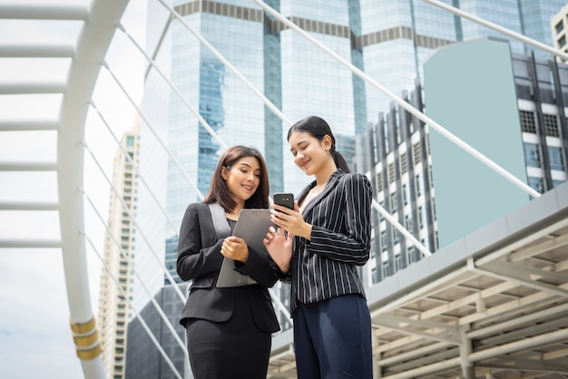 Due business woman in piedi utilizzando smartphone e discutere di fronte all&#39;ufficio. Concetto di lavoro aziendale.