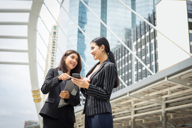 Due business woman in piedi utilizzando smartphone e discutere di fronte all&#39;ufficio. Concetto di lavoro aziendale.
