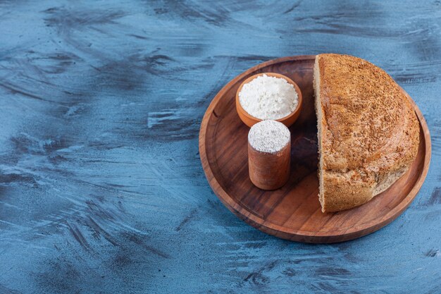 Due ciotole di farina e pane a fette su un piatto, sul blu.