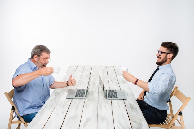 Due colleghi che lavorano insieme al progetto su sfondo grigio chiaro. Bevono caffè. uomo felice e uomo geloso. il concetto di concorrenza nel business