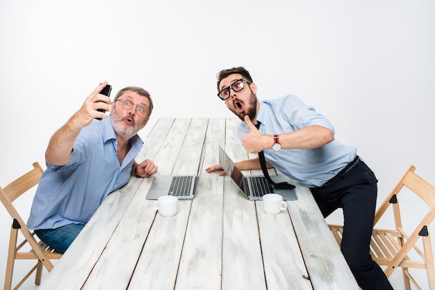Due colleghi che scattano la foto a loro stessi seduti in ufficio, hanno sorpreso gli amici con gli occhiali prendendo selfie con la fotocamera del telefono su priorità bassa bianca