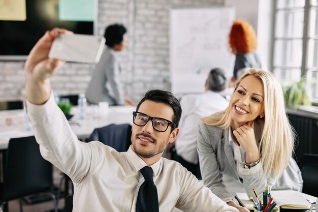 Due colleghi che si divertono in ufficio e si fanno selfie con il cellulare Ci sono persone sullo sfondo