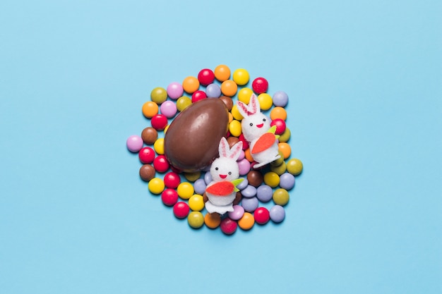 Due coniglietti bianchi e uovo di Pasqua al cioccolato su caramelle colorate gemma su sfondo blu