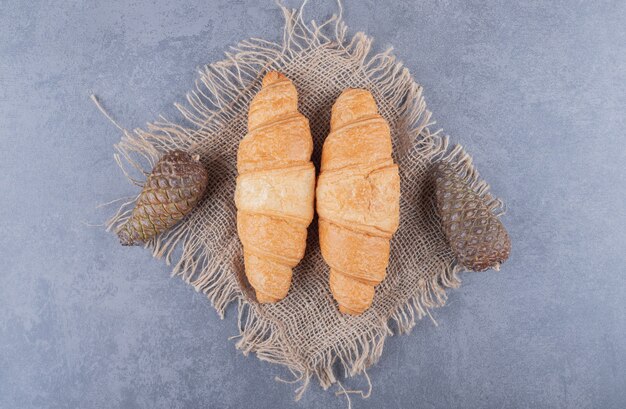 Due croissant freschi con pigne decorative su sfondo grigio.