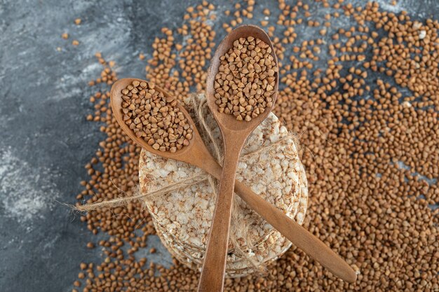 Due cucchiai di legno di grano saraceno crudo e pane croccante sulla superficie di marmo