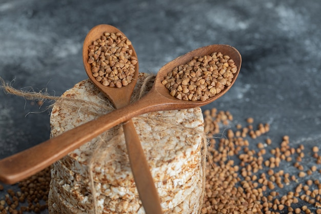 Due cucchiai di legno di grano saraceno crudo e pane croccante sulla superficie di marmo