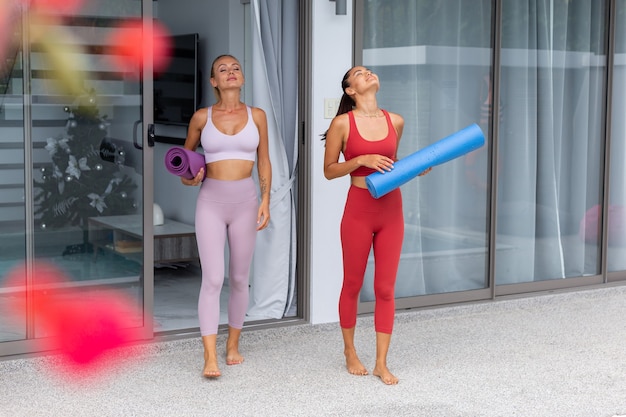 Due donne attive asiatiche e caucasiche vanno fuori a praticare yoga in villa di lusso a bordo piscina