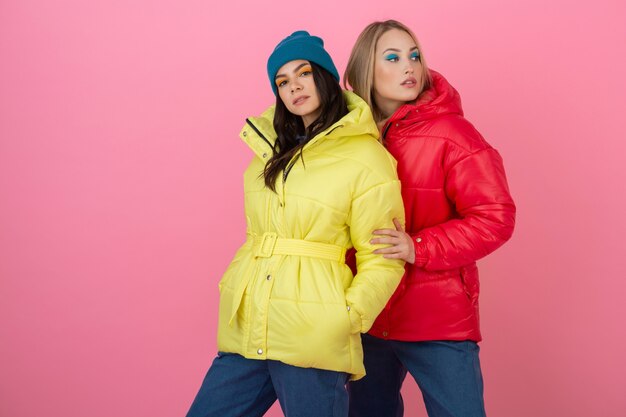 Due donne attraenti alla moda in posa su sfondo rosa in piumino invernale colorato di colore rosso e giallo, tendenza della moda vestiti caldi