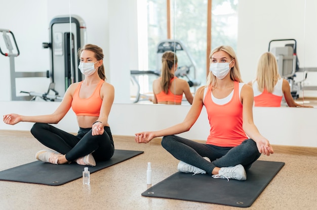 Due donne che fanno yoga in palestra con mascherine mediche