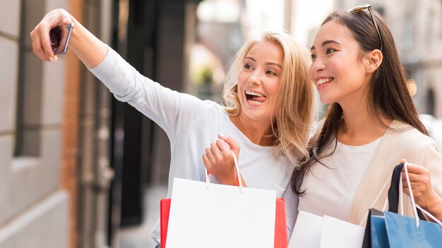 Due donne che prendono selfie con molte borse della spesa