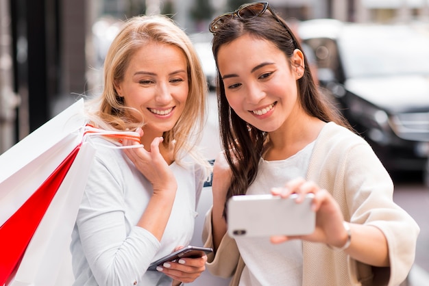 Due donne che prendono selfie tenendo un sacco di borse della spesa