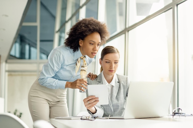 Due donne d'affari che collaborano mentre lavorano alla tecnologia wireless in ufficio