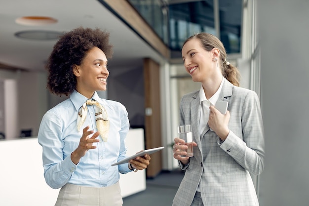 Due donne d'affari felici che comunicano stando in piedi in un corridoio