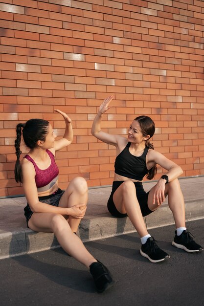 Due donne dopo l'allenamento urbano danno il cinque per ottimi risultati. Ragazze che si preparano a correre e si siedono per strada.